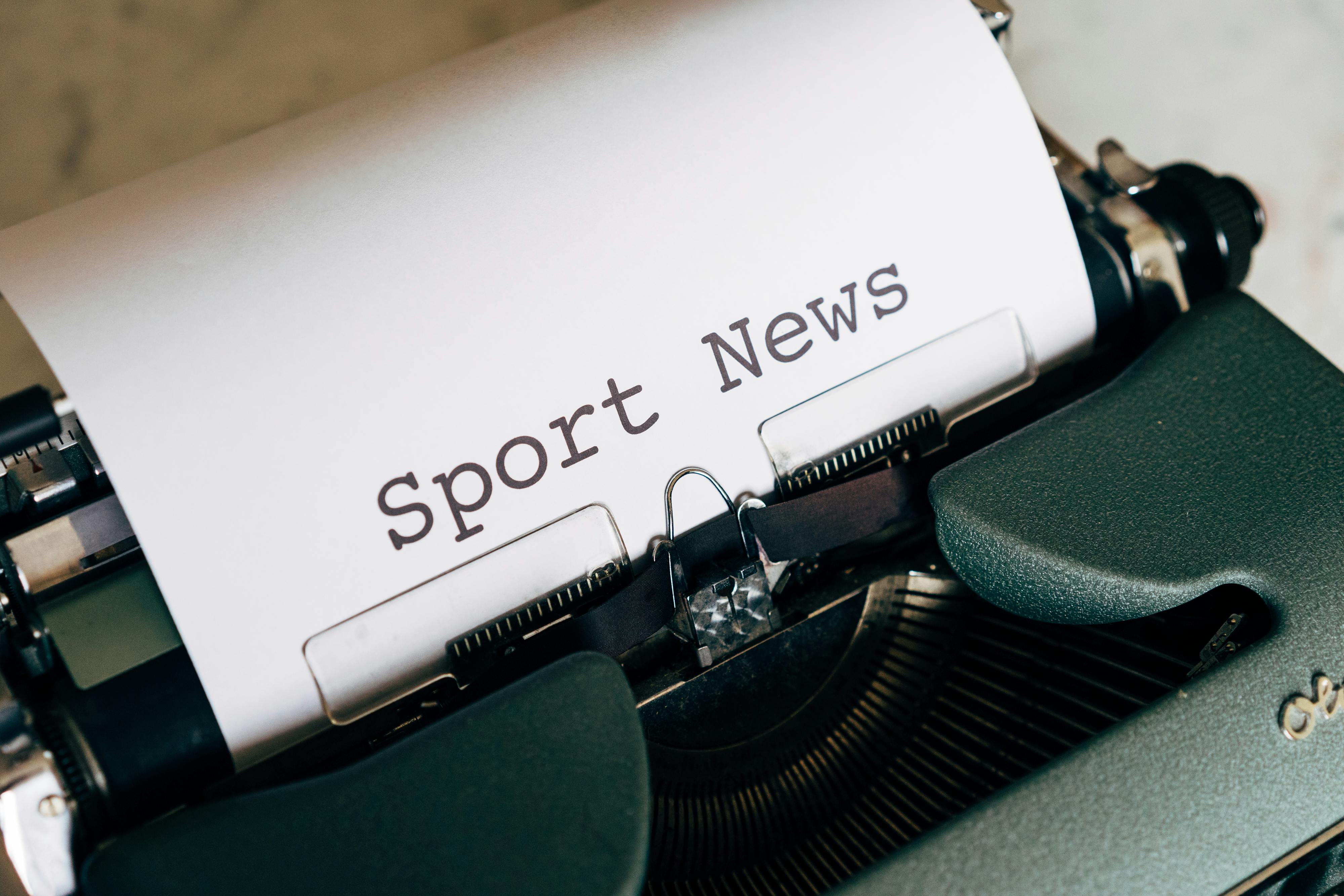 Close-up of a vintage typewriter with 'Sport News' typed on paper, evoking retro charm.